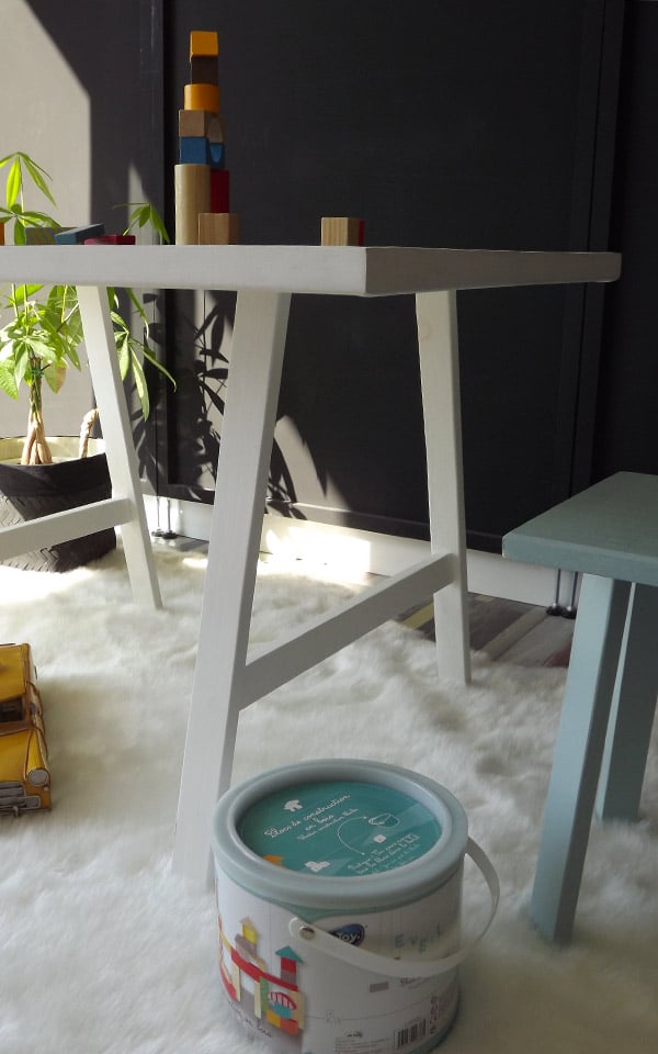 Table enfant avec 2 tabourets jaune et bleu. Cette table dispose d'un plan de travail en parquet stratifié. Certaines décorations sont de Maison du Monde ©