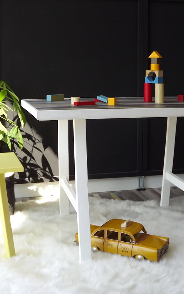 Table enfant avec 2 tabourets jaune et bleu. Cette table dispose d'un plan de travail en parquet stratifié. Certaines décorations sont de Maison du Monde ©